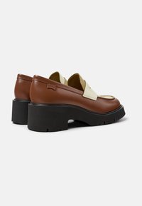 Bruine leren schoenen met een lichte crème accent, ronde neus, dikke zwarte hak en een Camper-logo op de zijkant. Textuur oppervlakte.
