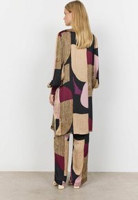 Multicolored patterned outfit featuring a long tunic and wide-leg pants. Materials include smooth fabric with abstract shapes in black, gold, and burgundy.