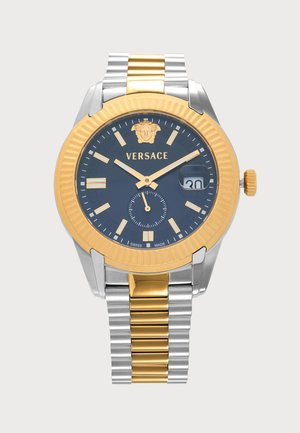 Montre-bracelet Versace avec bracelet en métal or et argent, cadran noir, index et aiguilles dorés, guichet date à trois heures et logo Méduse en haut.