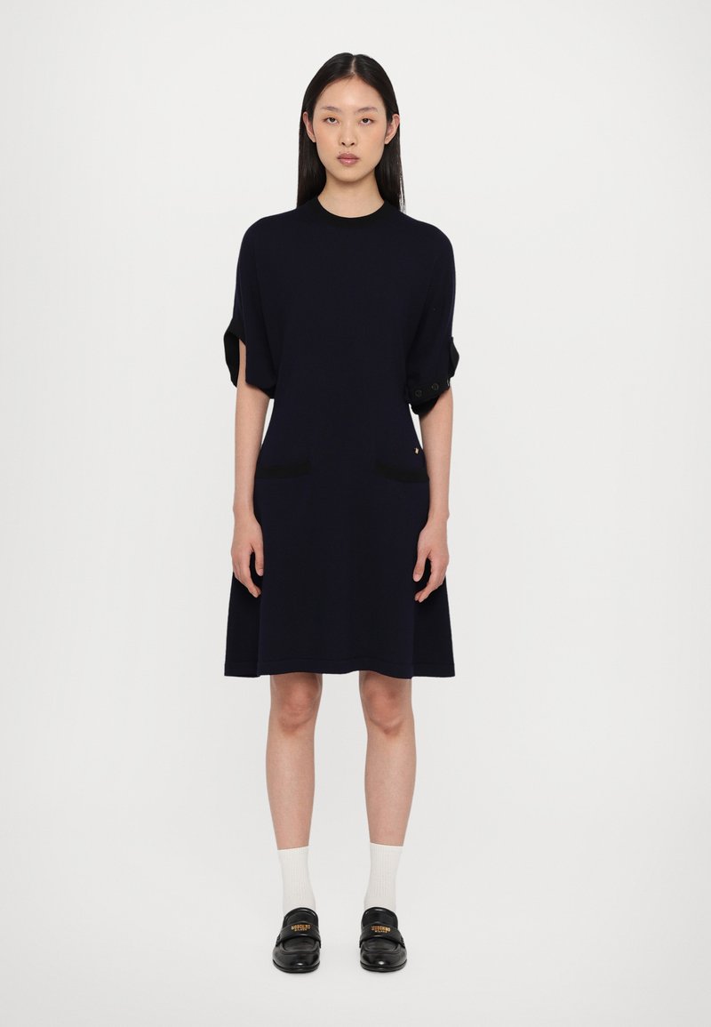 Robe navy à longueur genou avec des manches courtes, comportant deux poches avant et une coupe décontractée. Associée à des mocassins noirs et des chaussettes blanches.