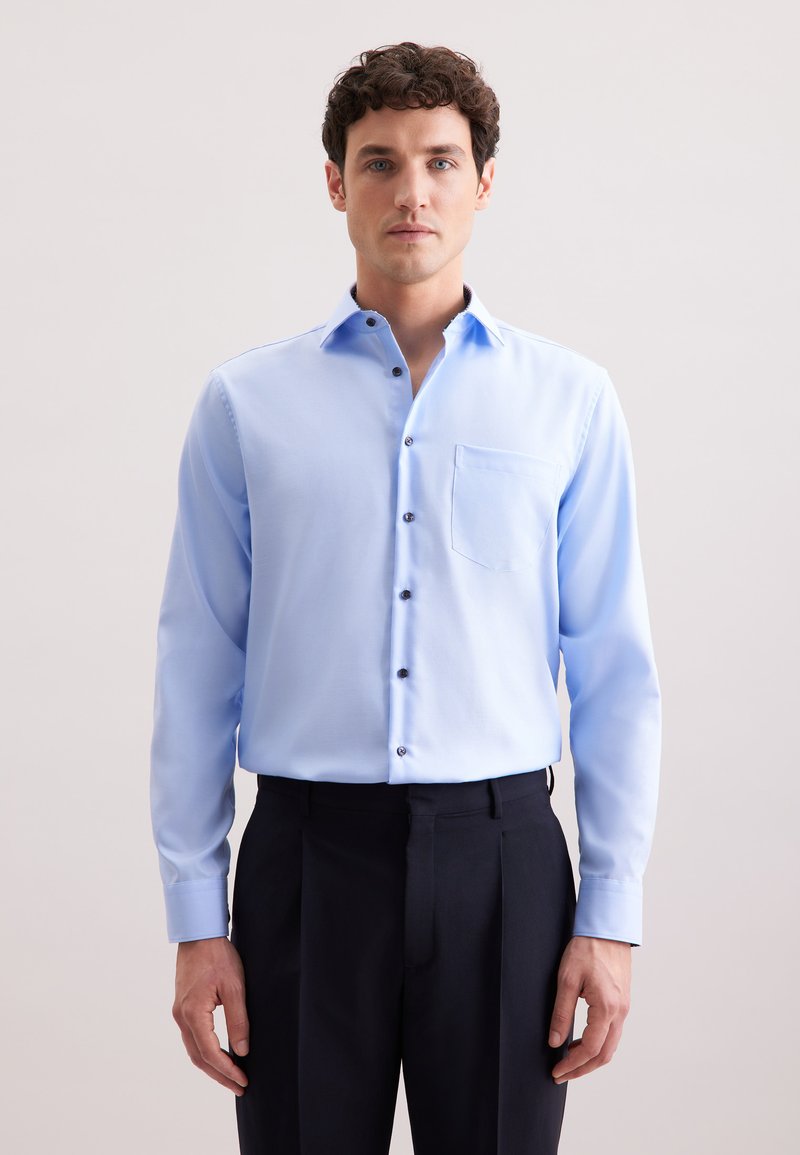Lichtblauw overhemd met lange mouwen, knoopsluiting en een enkele borstzak, en donkere knopen, gecombineerd met donkere broeken. Soepele stoftextuur.