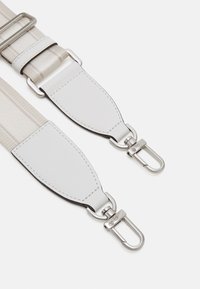 Cinghietta regolabile in tessuto beige con dettagli in pelle bianca, dotata di fermagli in metallo argentato e una texture liscia e piatta.