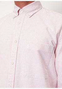 Chemise boutonnée à rayures roses et blanches, manches longues, col boutonné et poche poitrine avec un petit logo. Tissu texturé.