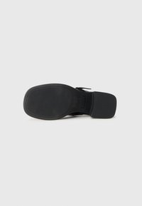 Black shoe sole with a square heel and horizontal ridges, lying flat on a white surface.