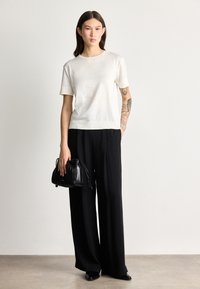 Top blanco de manga corta combinado con pantalones de pierna ancha negros. El conjunto incluye un pequeño bolso de cuero negro, con un acabado texturizado y un diseño ceñido.