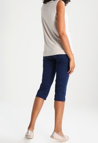 Ljusgrå ärmlös topp i kombination med marinkappor. Tyget verkar slätt, med en enkel design och en avslappnad passform; avlutad med slip-on skor.