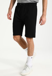 Shorts en coton noirs avec une taille élastique et un cordon de serrage, offrant une coupe décontractée et arrivant juste au-dessus du genou.