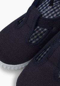 Zapatillas de lona azul marino sin cordones con aberturas elásticas, suelas de goma blanca y forro a cuadros en azul y blanco. Diseño duradero y ligero.