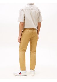 Beżowe chinosy o prostych nogawkach, wykonane z bawełny, zestawione z lekką, paskowaną koszulą z krótkim rękawem oraz białymi trampkami z akcentami.
