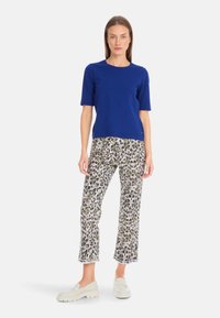 Blue short-sleeve top paired with white pants featuring a green and black animal print, complemented by cream-colored slip-on shoes.