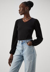 Svart topp med teksturert, puffede ermer som viser dyremønster; sammen med lyseblå, slitte jeans. Enkel sølvkjede.