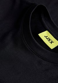 Κοντινό πλάνο σε μαύρο λαιμόκοψης μπλούζας με κίτρινη ετικέτα μάρκας ραμμένη στο εσωτερικό με το κείμενο JXX.