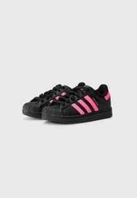 Sorte sneakers med tre vertikale rosa striper, strukturert tåhette og flat sort såle. Snøring er svart, med merkevare på siden.