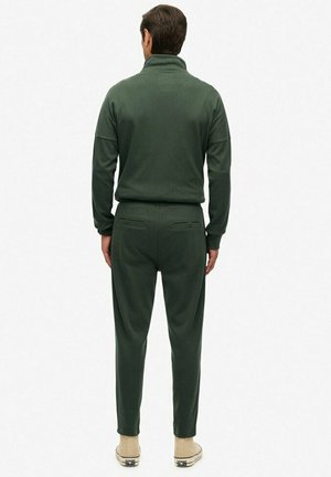 Tuta in tessuto verde morbido con colletto alto, vita elastica e tasche laterali. Presenta una vestibilità rilassata e pantaloni affusolati.