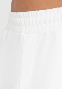 Witte sweatpants met een zachte, gladde textuur, een elastische tailleband en zijkantdetails. Close-up toont de tailleband en de kwaliteit van de stof.