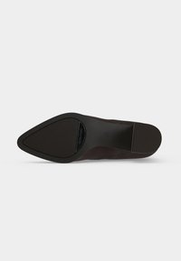 Semelle d'une chaussure marron à bout pointu vue de dessous avec des zones de grip texturées sur la pointe et le talon.