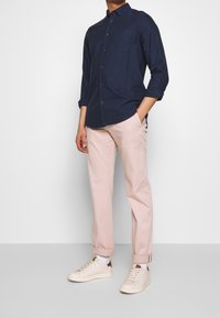 Granatowa koszula na guziki z długimi rękawami, zestawiona z jasnoróżowymi spodniami i białymi tenisówkami. Koszula posiada kieszeń na piersi i podwinięte rękawy.