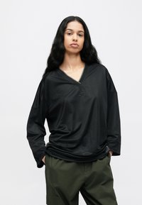 Μαύρο μακρυμάνικο τοπ με V λαιμόκοψη, λεπτή ριγέ υφή και λεπτομέρεια με λογότυπο, σε συνδυασμό με πράσινο cargo παντελόνι με πλαϊνές τσέπες.