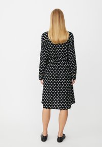 Czarna sukienka z geometrycznym wzorem w białe i jasnoniebieskie kolory, długimi rękawami i paskiem wiązanym w talii. Prosty, zwiewny krój.