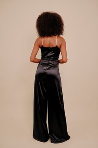 Μαύρη σατινέ ολόσωμη φόρμα με εφαρμοστό μπούστο, παντελόνια με φαρδιά πόδια και ρυθμιζόμενες λεπτές τιράντες με διακριτική λάμψη. Εμφανίζεται η πίσω όψη.