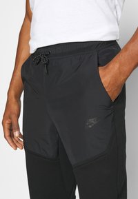 Černé šortky Nike s elastickým pasem, šňůrkou a bočními kapsami. Mají texturovaný materiál a černé logo na dolní části nohy.