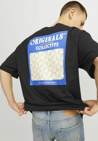 Juodas trumpomis rankovėmis marškinėliai su mėlyna stačiakampio grafika, kurioje užrašyta "ORIGINALS COLLECTIVE" ir tekstūrinis kreminės spalvos geometrinis raštas.