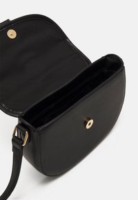 Sort læder crossover-task med en glat tekstur, magnetlukning og justerbar rem. Indvendigt har den flere rum til organisering.