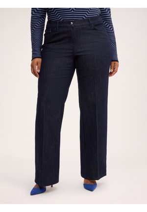 Plus-Size-Person trägt dunkelblaue Jeans mit weitem Bein, ein langärmeliges navy-schwarz gestreiftes Oberteil und blaue spitze High-Heel-Schuhe.