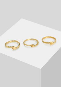 Tres anillos de oro: uno con un diseño en zigzag, otro con una textura de cuentas y otro con un patrón retorcido. Todos los anillos son finos y lisos.