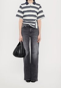 Personne portant un jean large gris et un polo à rayures noir et blanc, tenant un sac à main plissé noir à ses côtés.