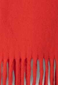 Piros gyapjú sál, bojtokkal a alsó szélén, amely puha textúrával és egyszínű megjelenéssel rendelkezik, minták vagy további díszítések nélkül.