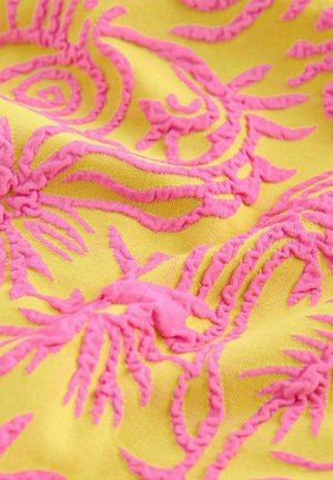 Tessuto giallo con ricami rosa intricati a motivi a spirale e foglie. La trama sembra morbida con dettagli di fili rialzati.