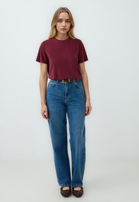 T-shirt di cotone bordeaux con maniche corte, abbinato a jeans in denim blu a vita alta e scarpe intrecciate marroni. Design e vestibilità semplici.