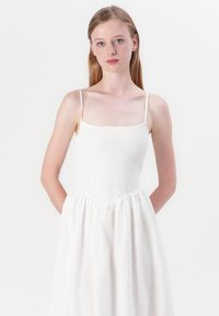 White dress with a fitted, textured bodice and a flowing, gathered skirt. Thin adjustable straps, lightweight fabric, and soft texture.