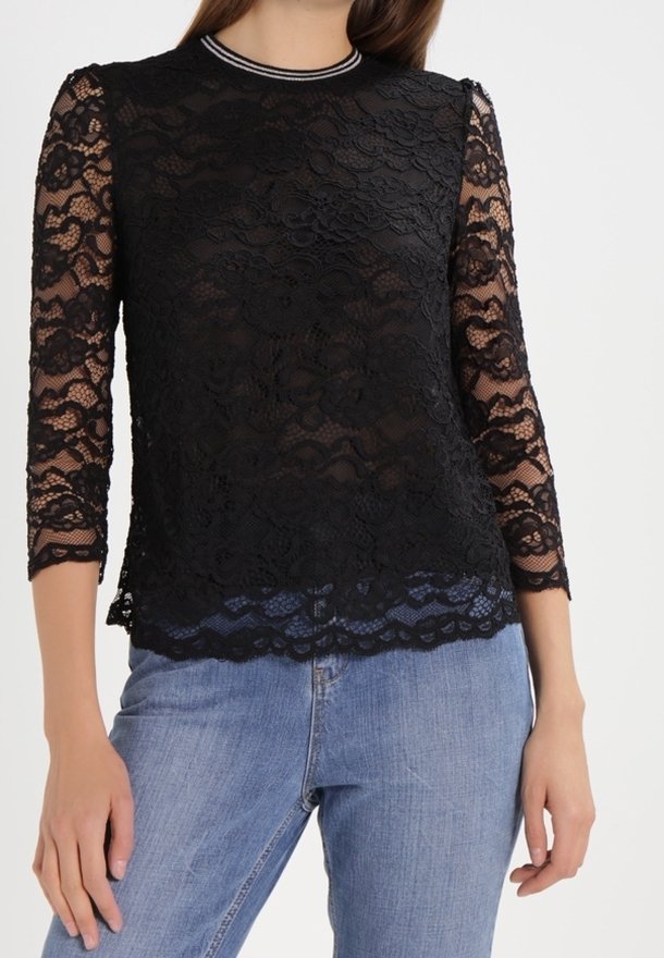 Top in pizzo nero con maniche a tre quarti e orlo scalloped. Presenta un colletto rotondo con rifinitura argentata a contrasto.