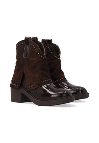 Brązowe zamszowe botki sięgające kostki z błyszczącym patentowym czubkiem, ćwiekowanymi akcentami wzdłuż górnej krawędzi oraz masywnym obcasem z pętelkami do zakupu.