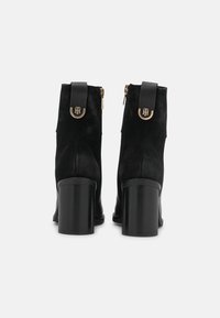Bottines en suède noir avec un large talon bloc, dotées d'une languette à l'arrière et d'accents en métal doré. Fermeture éclair sur le côté.