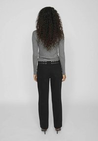 Jeans negros de tiro alto con corte recto, que cuentan con un detalle de cinturón con tachuelas y bolsillos traseros, combinados con una blusa gris de manga larga ajustada.