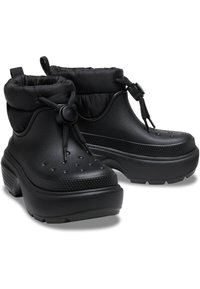 Botas de tobillo negras impermeables con parte superior acolchada, toggle ajustable, patrón perforado, suela gruesa de plataforma y acentos texturizados.