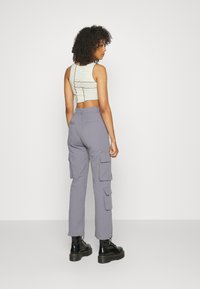 Hellbeige Cropped Top mit schwarzen Linien, kombiniert mit grauen Cargo-Hosen mit mehreren Taschen und schwarzen Plattform-Stiefeln.