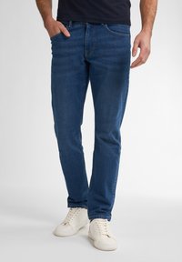 Jeans de denim azul oscuro con un corte recto, cinco bolsillos y un ligero efecto deslavado. Combinados con zapatillas blancas para crear contraste.