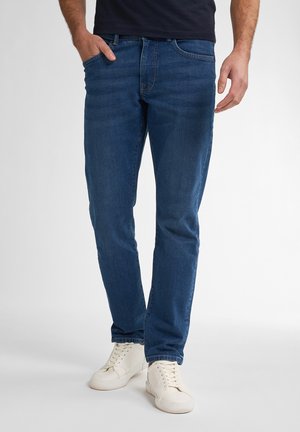 Donkerblauwe denim jeans met een rechte pasvorm, vijf zakken en subtiele wassing. Gecombineerd met witte sneakers voor contrast.