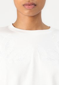 Witte katoenen sweatshirt met textuurrijke bloemenborduursel aan de voorkant, ronde halslijn en een eenvoudig ontwerp zonder extra accenten.