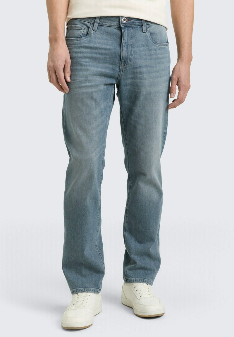 Jasnoniebieskie dżinsy z prostą nogawką, pięcioma kieszeniami i subtelnym przetarciem; noszone z białymi trampkami.