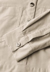Chemise en velours côtelé beige avec des boutons argentés portant la marque "Street One". Les détails incluent un poignet et une texture verticale subtile.