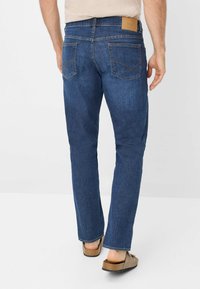 Jeans in denim blu scuro con taglio dritto. Le caratteristiche includono due tasche posteriori, cuciture visibili e una patch in pelle con logo sulla cintura.