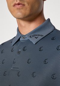 Dark blue polo shirt featuring vertical stripes and a subtle logo pattern. Textured fabric with a collar, buttons, and embroidered branding.