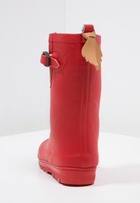 Rød gummistøvle til regnvejr med en tekstureret overflade, en bageste spænde detalje og et dekorativt tan lædermærke på hælen.