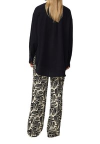 Zwart gestructureerd oversized shirt gecombineerd met crèmekleurige broek met een zwart bladrandpatroon, met een losse pasvorm en een ontspannen ontwerp.
