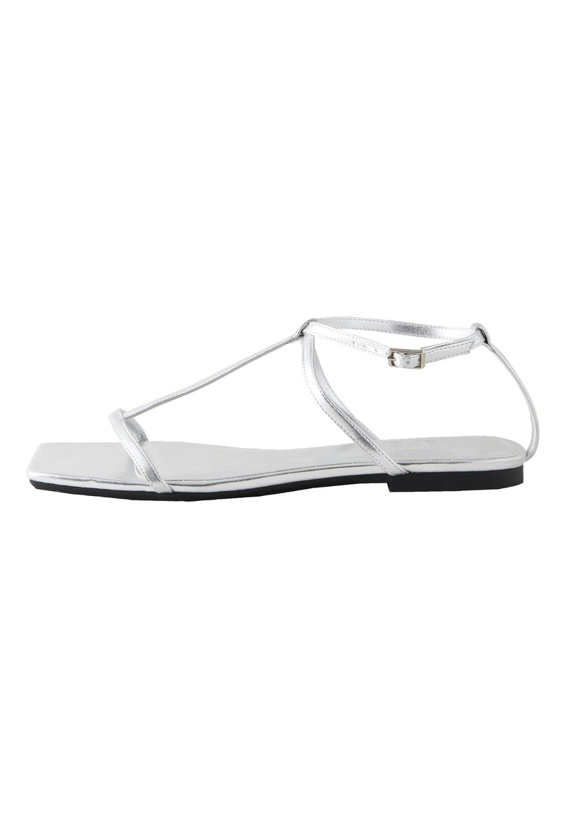 Sandalia plana plateada con diseño de T-strap, hecha de material sintético, con punta cuadrada y un cierre minimalista con hebilla en el tobillo.